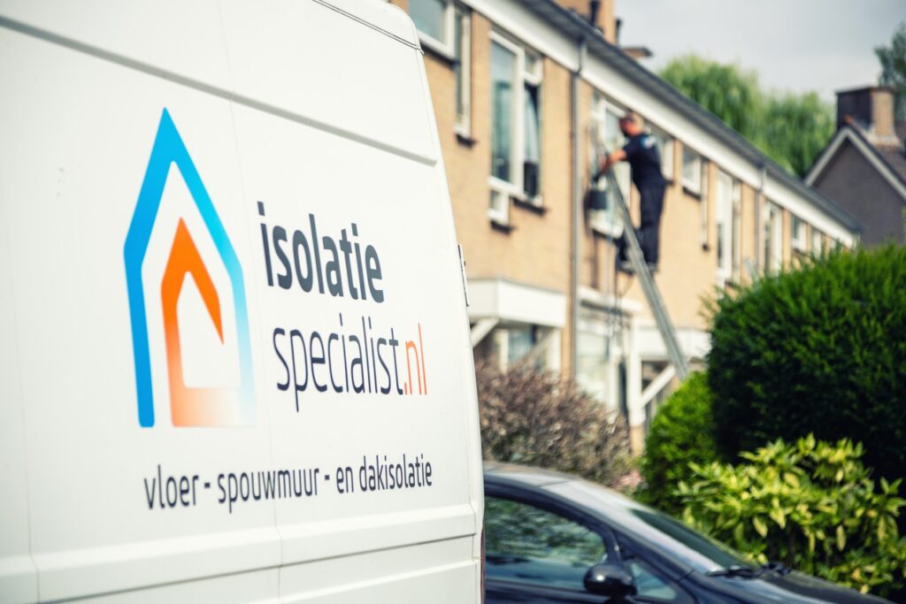 Bedrijfsbus van Isolatiespecialist.nl in een woonstraat, een monteur isoleert op de achtergrond een spouwmuur
